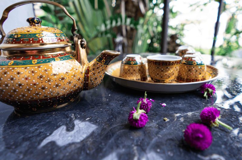 An antique Benjarong porcelain tea set with intricate gold detailing, elegantly displayed on a stone table, showcasing the rich heritage of Thai ceramics.