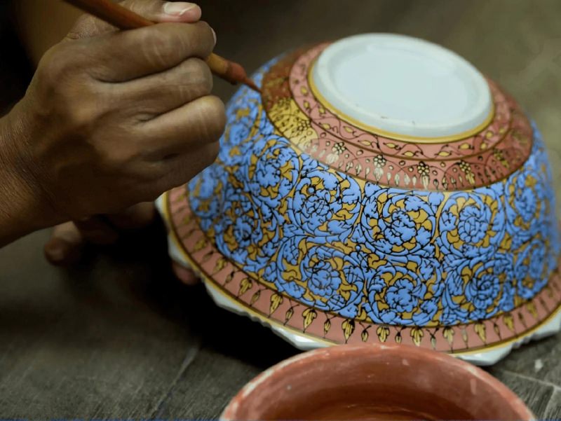 A Thai artisan meticulously painting delicate patterns on a Benjarong plate, showcasing the intricate hand-painted details that define this traditional porcelain art.