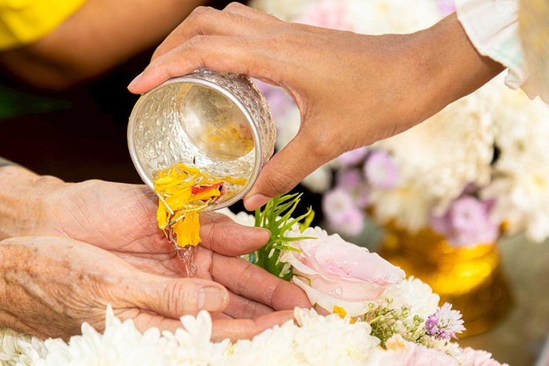 A serene moment of a child or young adult pouring water into the hands of an elder or a monk with jasmine flowers in the bowl.