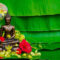 A hand pouring scented water with flower petals over a Buddha statue as part of a traditional Songkran blessing ritual in Thailand.