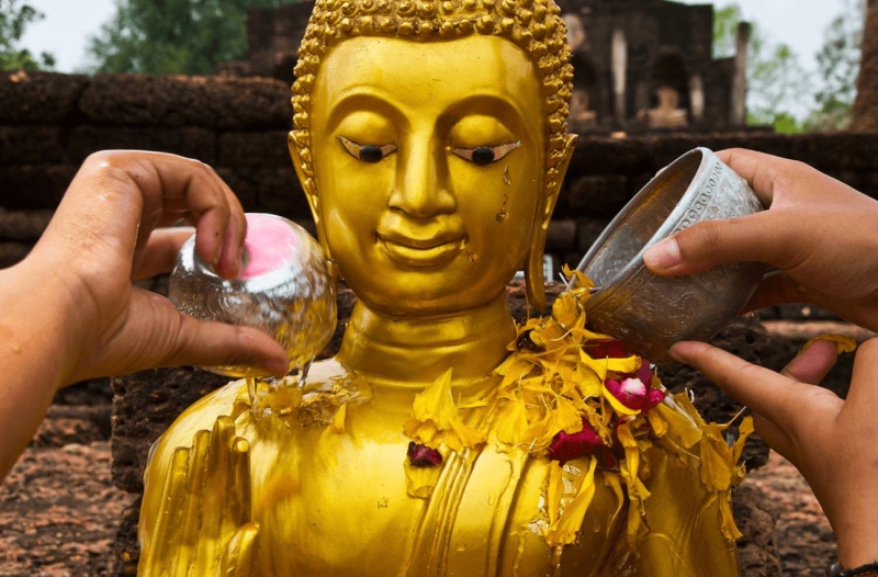 People gently pouring water over Buddha statues or over elders' hands in a traditional blessing.